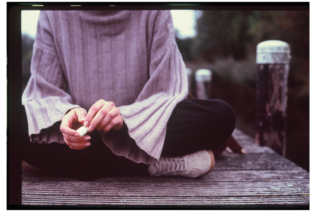 Person sitting on a wooden dock with hands clasped.
