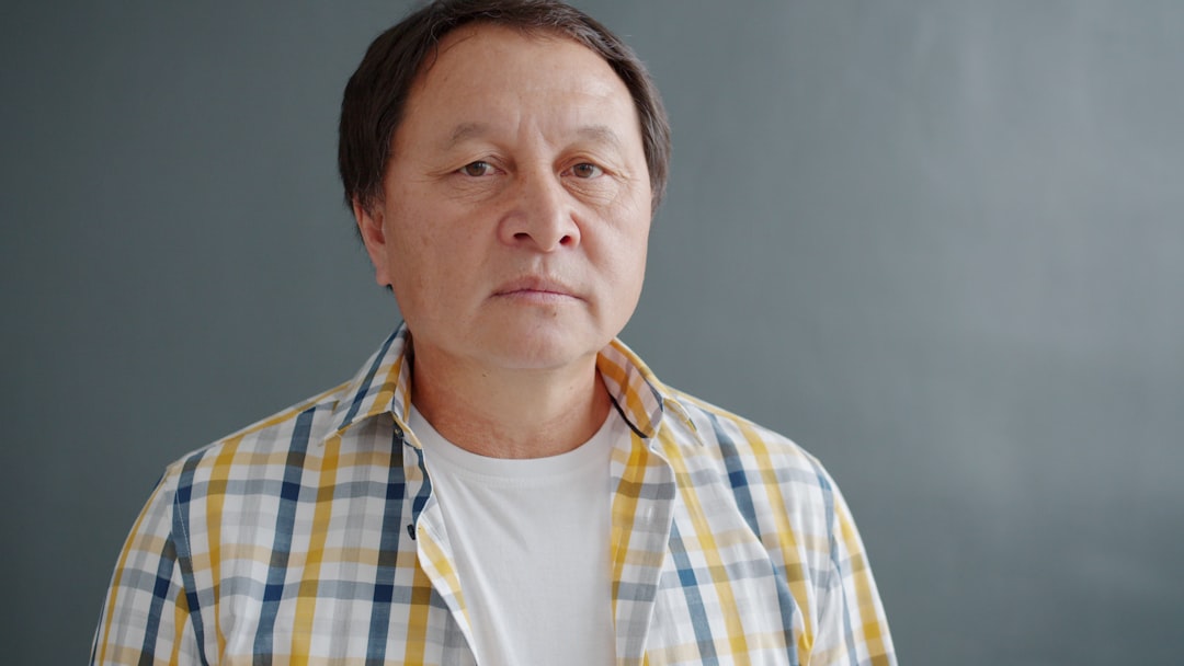 Elderly asian man in plaid shirt against gray background