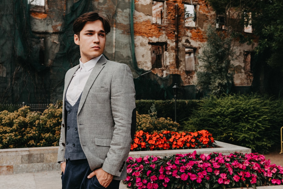 man in gray suit jacket standing near red flowers